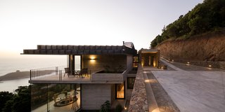 The upper volume—where the garage, kitchen, service areas, two bathrooms, and a patio are located—is a half-submerged body of stone set within the upper section of the slope. 
