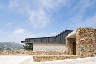 This stone volume emerges from the topography like an ancestral cave, with its mouth serving as the entrance to the house. 