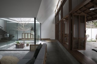 On the ground floor of the three-level house is a front yard and parking area with a few tall trees. 