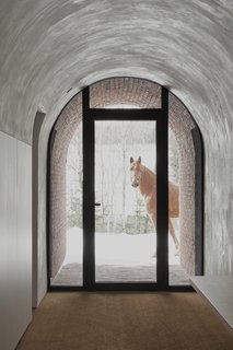 Wide, low ceilings frame views toward the horse arena, while also creating visual tension between the interiors and the lush landscape outdoors.