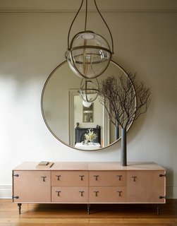 A BBDW leather credenza and round mirror, along with a chandelier by Urban Electric Kensington are located in the entry hall.