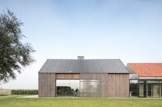 Streamlined sections of metal-framed windows with triple glazing stylishly connect the brick and wooden volumes. 