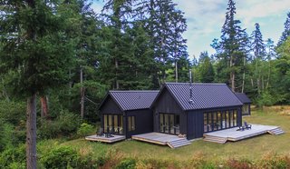 Taking inspiration from the tradition of the Danish sommerhus, each volume is a simple, gabled form, clad in dark gray-stained cedar siding with standing-seam metal roofs that mirror the vertical grooves in a similar shade. 