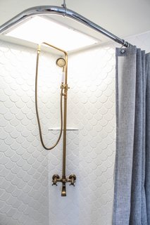 Major alterations were also made in the bathroom. The tired, plastic shower surround was removed and replaced with beautiful scalloped tiles from Floor & Décor, and a gold-colored shower head, purchased from Amazon, adorns the compact shower area. A ceiling-mounted shower rod and Target shower curtain replaced the heavy, dated shower doors that existed.