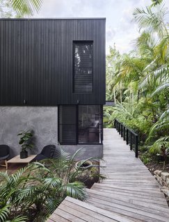 On one side of the home is a boardwalk that runs alongside verdant tropical plants. This boardwalk takes residence from the interior of the house, and goes out to the rainforest.