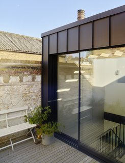 The upper floor has been set back at the front to make space for a another terrace with large potted plants.