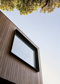 The upper section of the façade is clad in timber, and features large steel-framed windows that extend slightly beyond the siding.