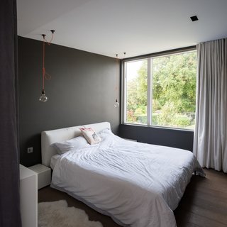 In this muted, gray bedroom, two Edison bulbs are suspended from the ceiling with bright, orange cords, lending a hint of color that instantly adds character and intrigue to the space.