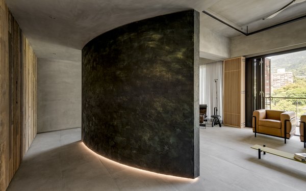 The gray-black structure in the middle of the home has been cladded in rusted metal and gold foil on one side to appear weathered and aged.