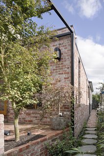 From the garden, the new extension was designed as a pair of interlocking volumes—a pitched, timber-clad wing that overlaps a smaller mass of salvaged brick. 