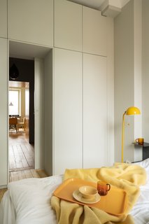 A bedroom wardrobe wall completes the renovation. Despite the more subdued color, yellow accents continue the apartment’s lively palette.