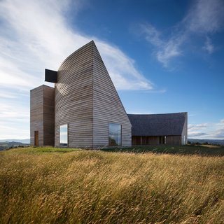 Set on an expansive meadow and overlooking the sea, Rode House is a semicircular residence on Chiloé Island featuring a dramatic, sloping roof that extends over an interior courtyard. Pezo von Ellrichshausen is a Chilean firm known for their arresting, geometric architecture. In true form, the striking, semicircular residence boasts a roof that drops steeply to form two sharp peaks at either end.
