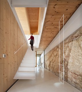 Embraced by a rocky terrain, the three rectilinear volumes of this house spreads interior spaces vertically over three levels, and horizontally over three enclosures. The residence, built from natural materials—some of which was excavated from the site itself—resembles a cavity within a monolithic stone quarry.