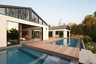 A bridge traverses the pool, connecting to a lower lounge deck and grassy yard. The home includes a guesthouse with a flexible space for a studio, gallery, gym, or home office.