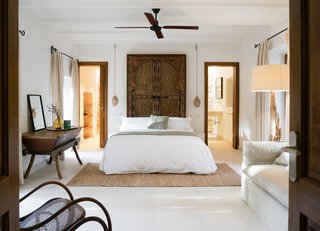 Two doors in this bedroom aren't symmetrically located, but by using matching wood frames, a centered bed with centered light fixtures, and matching window treatments, the discrepancy in the doors is rendered almost indecipherable.