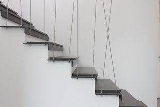 9 Unique Stair Railings - Photo 1 of 9 - In Geneva, an existing wooden stair is transformed with a steel tread topped with a plank of concrete. The distinctly modern feel extends to the steel tension rods that cross each other to create an irregular pattern.
