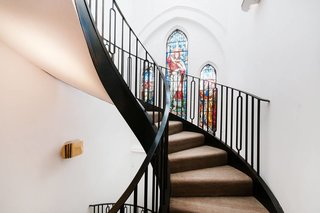 In the London neighborhood of Kenmont Gardens, a brick church's stained-glass windows provide a pop of color. It contrasts with the surrounding stark white walls and black powder-coated steel spiral staircase that connects the open-plan main level of the home to the bedrooms on the upper floors.