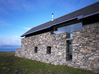 The newly constructed wing consists of a combination of stones from existing walls on the property, wood siding, glazed panels, and a new roof.