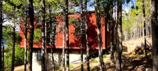 Siting closely within the surrounding pine forest, the Weehouse designed by Alchemy Architects and constructed by Irontown Homes rest only one half hour up the mountain from Boulder, Colorado. The tight driveway and secluded mountainside locale created an interesting delivery in which the modules were lifted by crane over the treetops and set into place. The pre-finished steel siding has been joined by a special fire-protective shell due to lying in a high-risk fire zone. The plethora of windows allow for natural sunlight to illuminate the warm, open interior.
