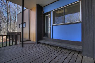 The exterior is clad in "Breuer blue" panels, tongue-and-groove vertical cypress siding, and generous expanses of windows with curated views to the landscape beyond.