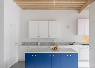 The kitchen's white palette allows the bright blue cabinets and gold hardware to stand out.