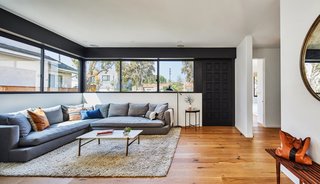 The main living space on the ground floor is located directly off the front door. It has a long horizontal window on two sides. The custom wood door is painted in Farrow & Ball "Pitch Black" with Emtek "Davos Tubular Marmont" mortise hardware and a US Black finish.