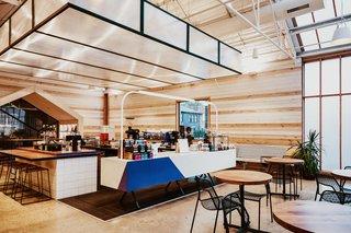 The light-filled, wood-clad flagship of Greater Goods Roasting in Austin features various types of seating including wood tables with black metal mesh chairs, wood benches, high stools, and plush armchairs and sofas. 