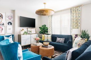 This living room designed by interior designer Veronica Solomon incorporates multiple patterns and bold colors that manage to not overpower each other because of the room's high ceilings, light-colored walls, and simple but statement light fixture at the center of the space.