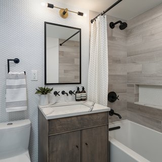 Interior design firm Eneia White Interiors established a modern twist on the classic penny round in this bathroom, pairing matte-black finishes with warm grays to create a clean and timeless aesthetic. 