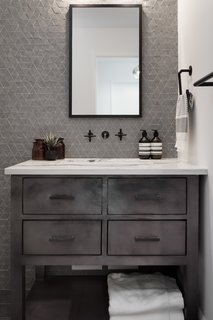 Textured accent walls, masculine metals, and wall-mounted fixtures create a spa-like retreat for a classic gentleman’s bathroom designed by Eneia White Interiors. 
