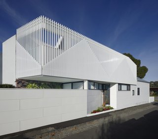 The street wall, new addition, and existing building are all united in their color palette of shades of white, but are distinct in their materials, shape, and joint patterns. The street wall and existing building have a horizontal emphasis, while the second floor's addition has a vertical one.
