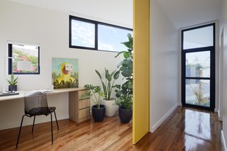 A large sliding door closes off a small home office, which takes advantage of its irregular shape by placing windows and plants near the corner.