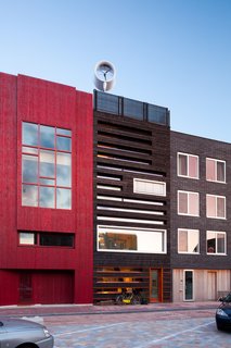 Along with the house's shou sugi ban front, the wood is layered with bright orange planks. Solar collectors, which consist of double-glass tubes that minimize heat loss, form a cornice on the front facade of the house. A wind turbine is on the roof.