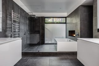 In this master bathroom, which is complete with a soaking tub, a linear fireplace, and floating vanities, the floor and walls are covered with large-format Italian porcelain tile from Emil Ceramica.