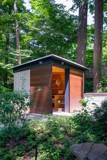 Designed to complement the existing adjacent home on the property, this modern gardening shed uses landscaping and terraced steps to create a pathway between the two buildings. Mixing horizontal and vertical wood planks gives the exterior of the shed a more dynamic facade, while exterior light fixtures provide necessary lighting at night.
