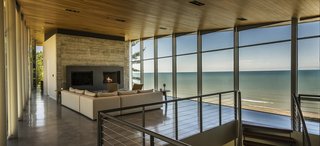 9 Marvelous Waterfront Homes - Photo 8 of 10 - Nestled between the sand dunes of Lake Michigan to the north and a steep wooded terrain to the south, the two-level home opens and connects to both environments. With the shifting sand dunes creating the topography of the site, the board-formed concrete base recedes into the rising woods while the all-glass living room and master suite above become a raised platform, or aerie, with views of both breathtaking landscapes.