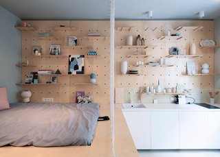 A knotted curtain bisects the sleeping area from the kitchen, which contains concealed and exposed storage units, as well as a small circular dining table.
