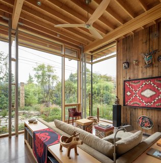 Defined by a soaring 16-foot-tall ceiling, the open-plan living room, kitchen, and dining area at the heart of the home, and overlook southeast views of gardens through walls of glass. 