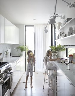 These 30 White Kitchens Are Anything But Ordinary - Photo 14 of 30 - The narrowness of the house required the design to make effective yet frugal uses of space. Precise positioning of walls, doors, and windows were crucial as each floor was planned to serve a purpose. The first floor is a continuous public space with a living room, dining area, kitchen, and library opening to gardens in the front and back.