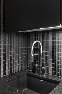 A minimalist black-and-white aesthetic is kept in this apartment kitchen, where elongated black tile is contrasted with lighter gray grout. The countertops are dark soapstone and the cabinets are a dark green-black.