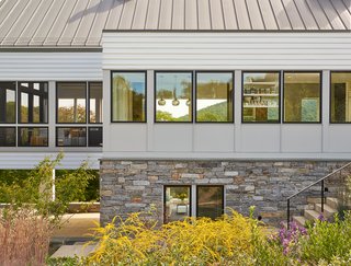 According to the architects, the screened porch panels (on the left) were site-built by the contractor to have similar dimensions as the Marvin windows (to the right). Dramatic black sashes unite the facade. Thin mull covers between window units blend with the exterior siding, "which afforded a consistency that we were after," said Wiedemann. Native stone on the foundation is similar to old Virginia farmhouses.