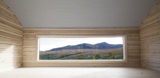 The panorama window in the barrel-vaulted living room offers a dramatic tableau. "The low position of the window emphasizes that this is a room to sit and relax," says the architects. This room was built with 19th-century notched logs.