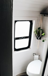 The bathroom hosts a composting toilet from Nature's Head and is spruced up with white wall paneling and a black-framed window.
