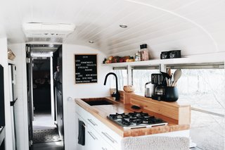 In the kitchen, white cabinets are combined with black accents and a butcher block countertop, including the sink basin and faucet. Windows at the counter bring in lots of natural light.