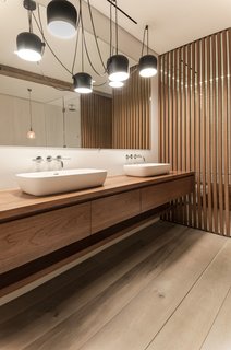 In the master bathroom, the teak vanity and wood screens were designed by Isaac-Rae and custom built by a furniture maker. The sinks by Apaiser were also made custom. The lighting is by Flos.
