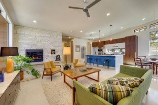 The open-concept living, kitchen, and dining area has terrazzo floors and a stone fireplace with a floating bench. The kitchen island is wrapped in quartz and illuminated by custom pendants from Hip Haven, a lighting designer based in Austin.