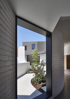 The architects located a new kitchen and dining space in the northern part of the addition. A curving corridor connects the original house to the new kitchen and dining space. Expansive openings in the hallway look into the new enclosed courtyard.