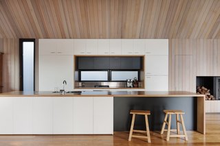 A streamlined kitchen is defined by its white cabinetry against the surrounding cedar walls. The floor is composed of Ash wood.