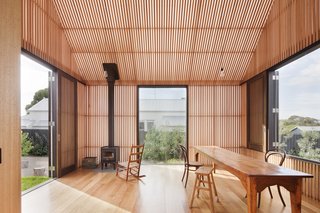 The white polycarbonate structure functions as a more protected version of a porch. Timber battens provide shading and cross ventilation. "In this case, the building is entirely clad in a triple skin, translucent polycarbonate cladding system with the inner skin entirely clad with timber battens," say the architects. "This space provides cool, shaded, ventilated space in summer (doors open) and a warm, passively heated space in winter (doors closed)."