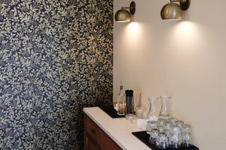 The dark-hued wallpaper from Rifle Paper offsets the brass sconces from Schoolhouse Electric.